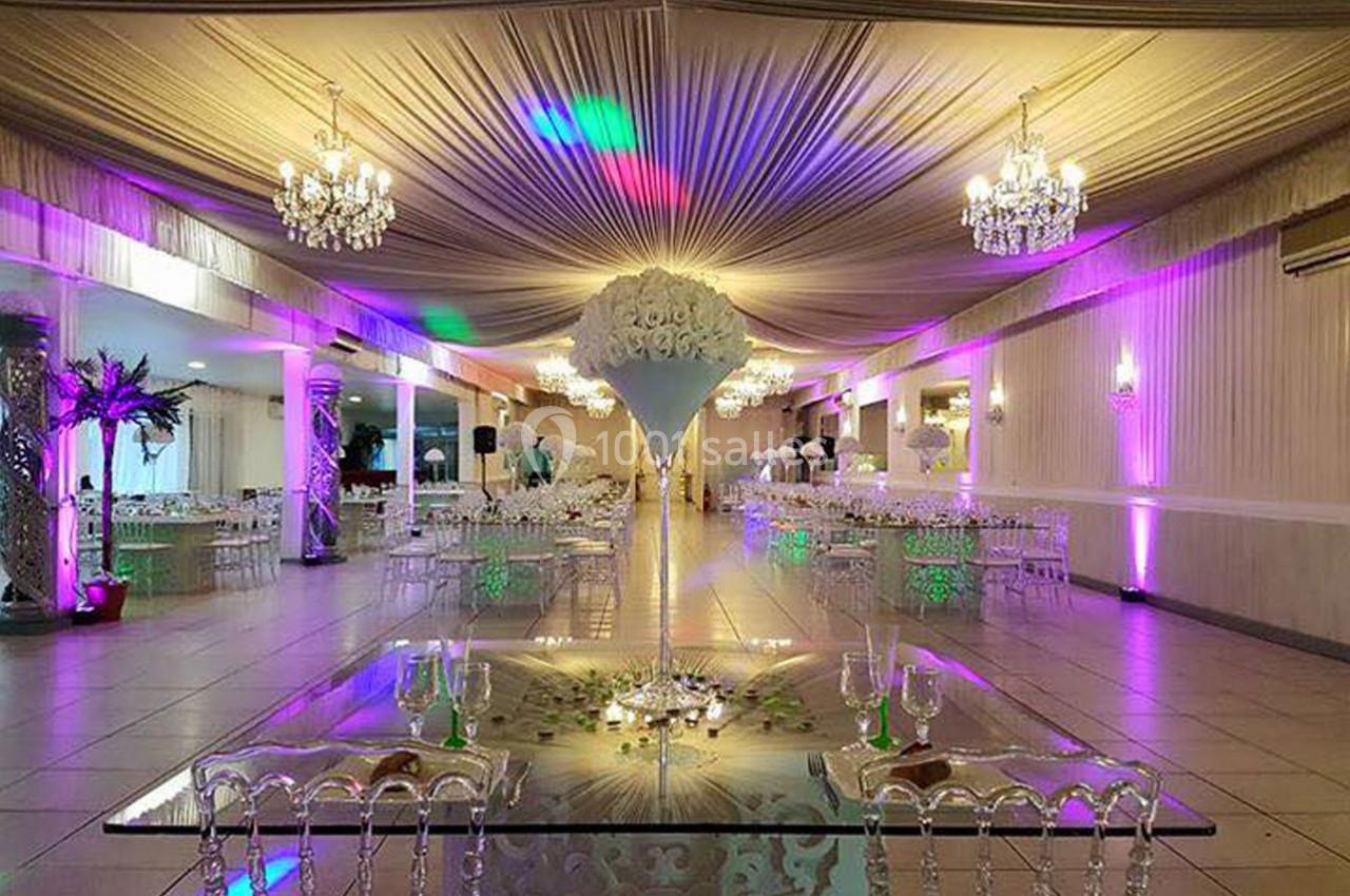 Salle de réception élégante avec tables dressées, lustres suspendus et éclairage coloré.