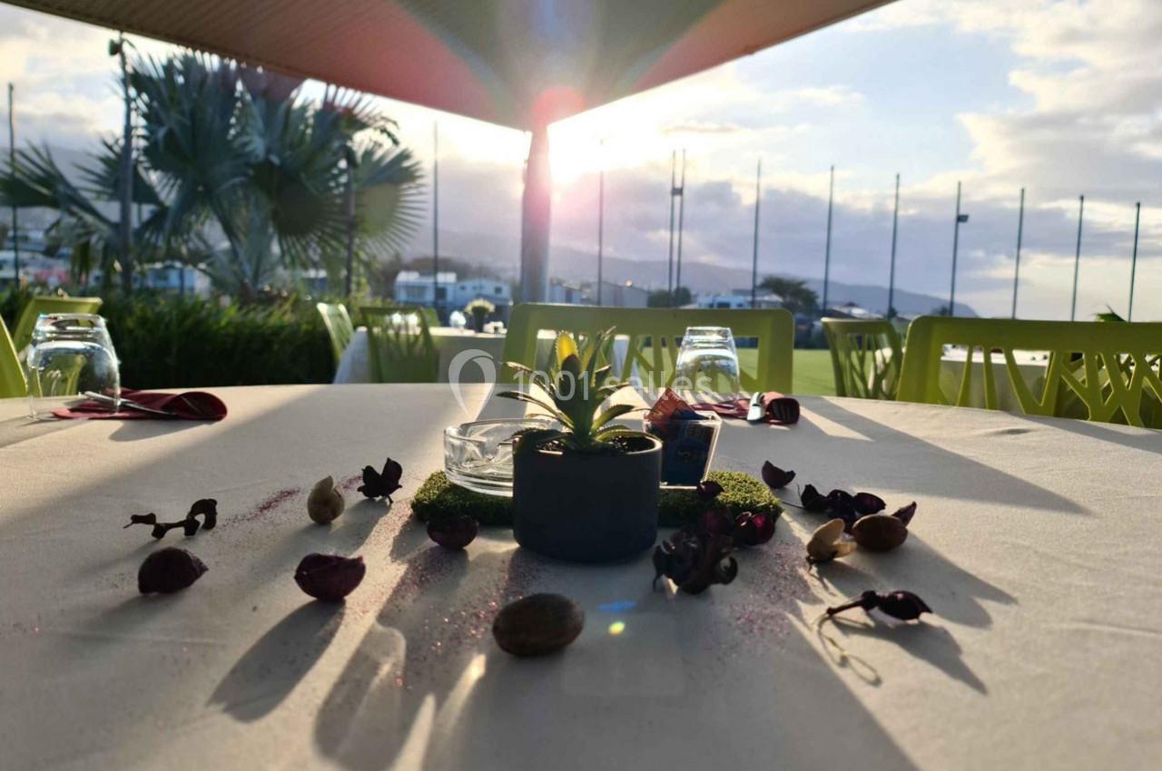 Table extérieure décorée avec des plantes et pétales, éclairée par le soleil couchant près d'un port.