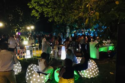 Groupe de personnes rassemblées dans un jardin éclairé par des guirlandes lumineuses lors d'un événement nocturne.