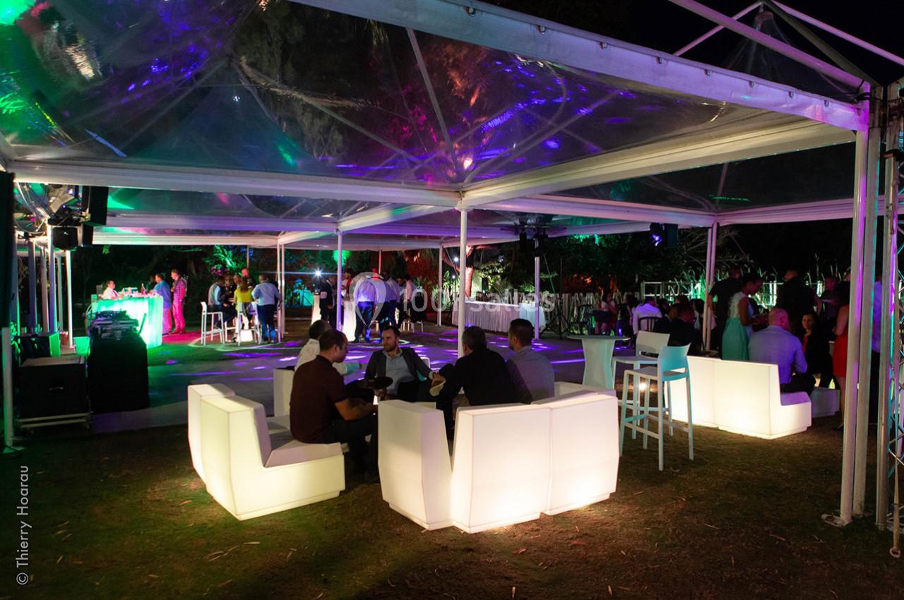 Des invités discutent sous une tente éclairée lors d'un événement nocturne en plein air avec bar et éclairages colorés.