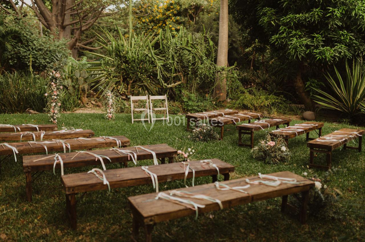 Bancs en bois disposés en extérieur sur une pelouse, entourés de végétation, pour une cérémonie en plein air.