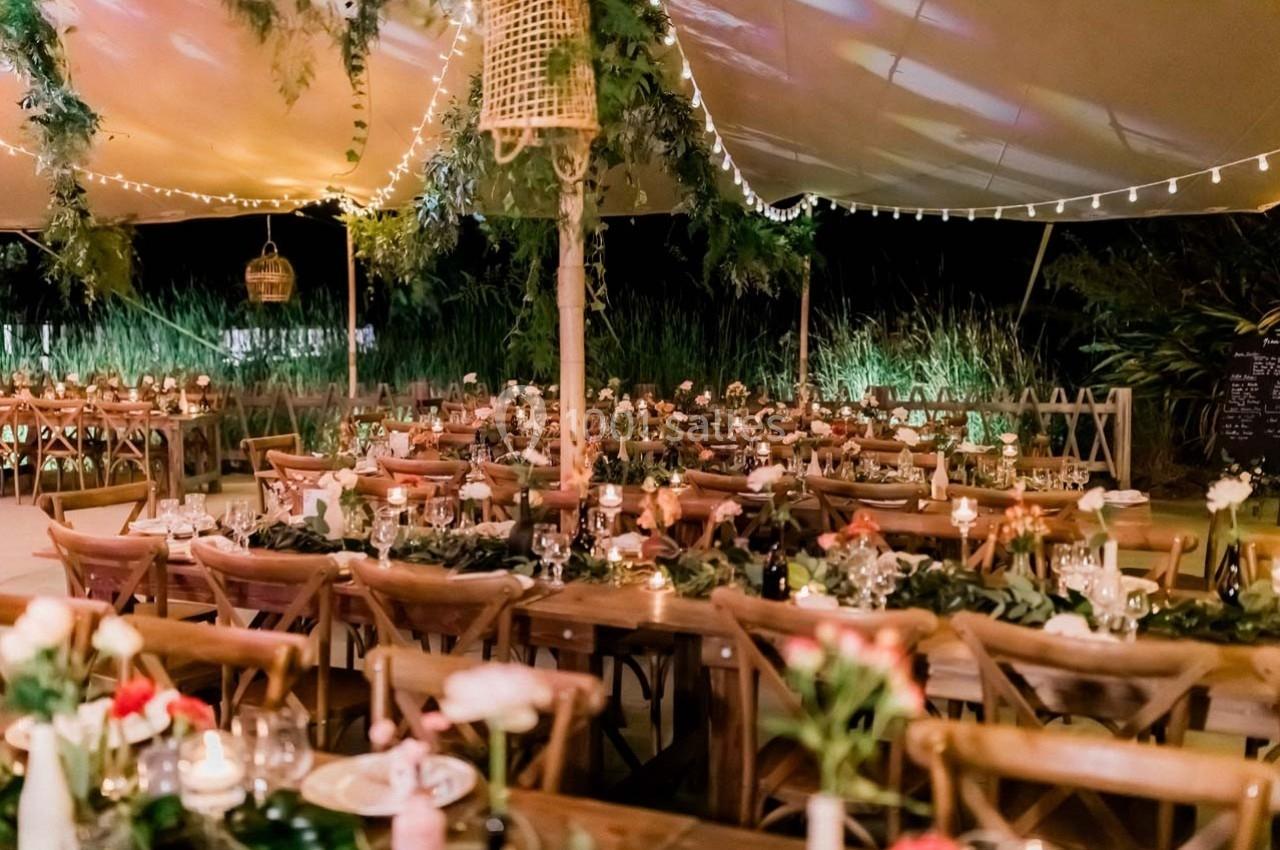 Salle de réception en plein air décorée de guirlandes lumineuses, tables en bois et arrangements floraux.