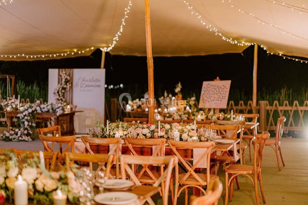 Salle de réception en plein air décorée de guirlandes lumineuses, tables en bois et arrangements floraux élégants.