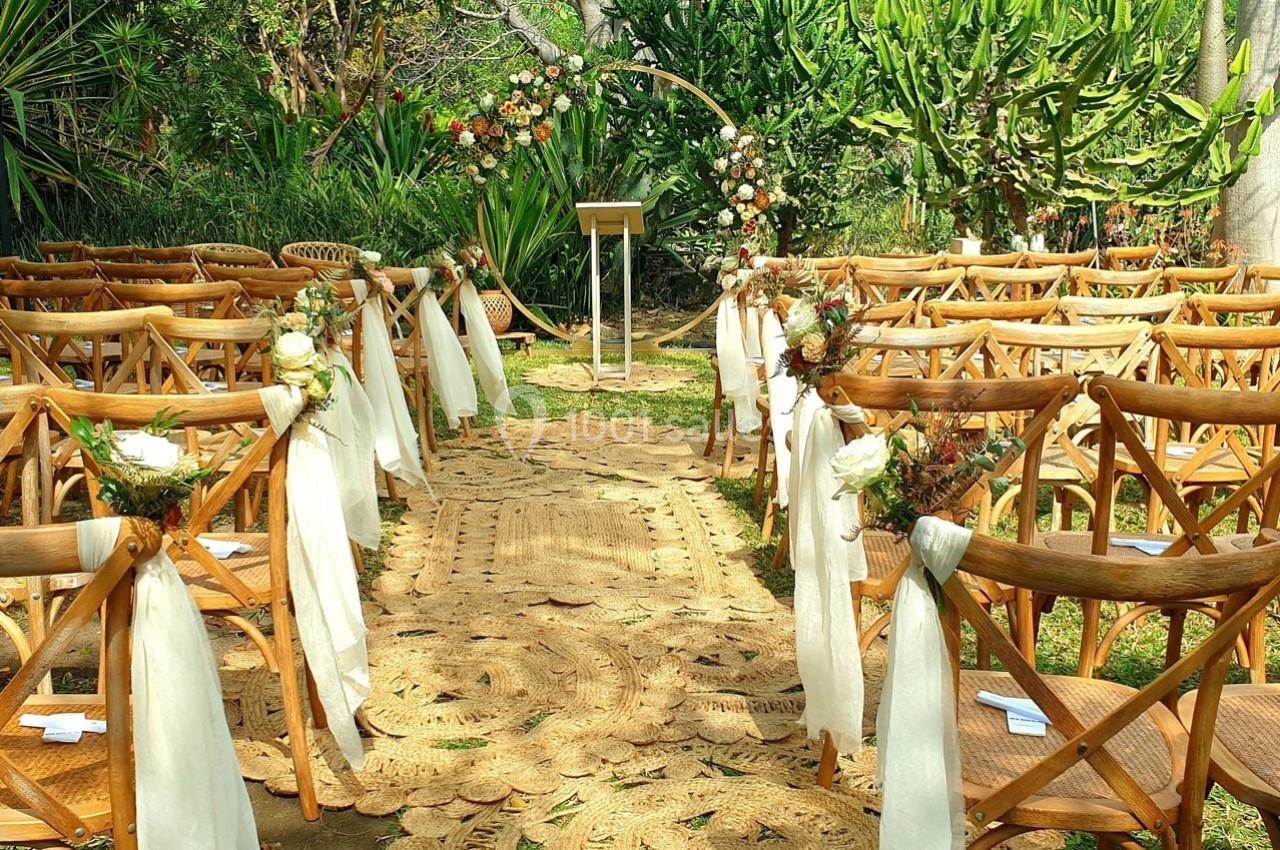 Chaises en bois décorées de fleurs et rubans, disposées en allée centrale pour une cérémonie en extérieur.