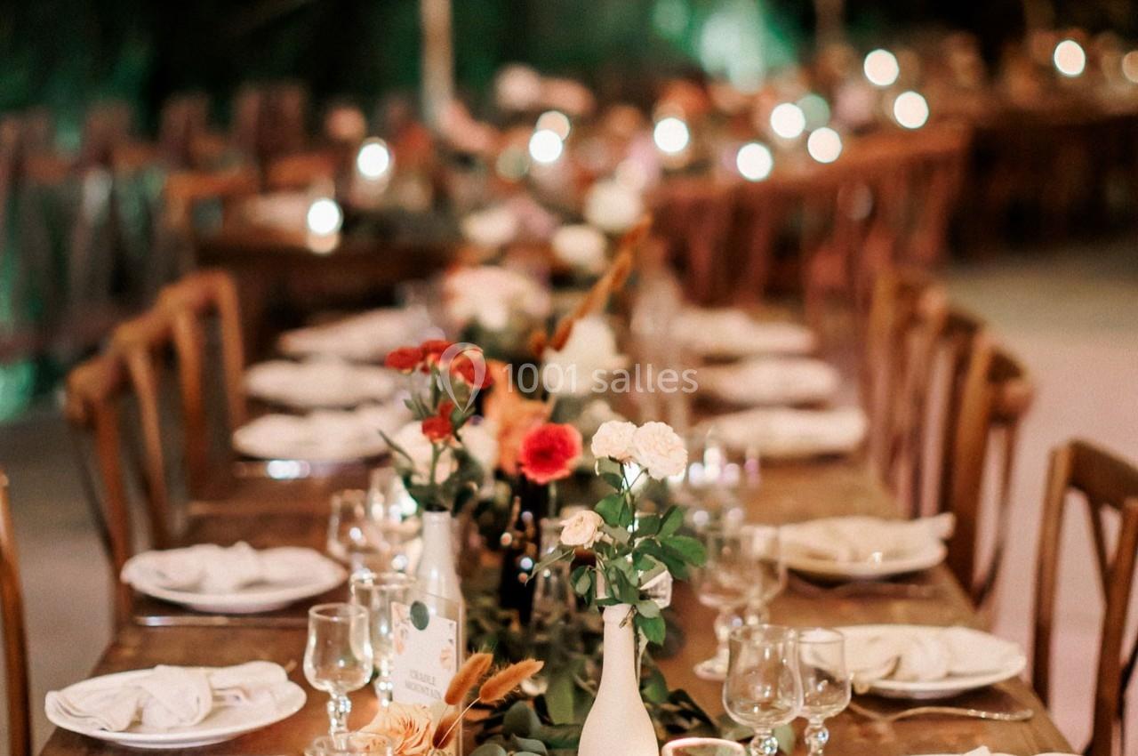 Table en bois décorée avec des fleurs, vaisselle blanche et verres, éclairée par une lumière tamisée en arrière-plan.