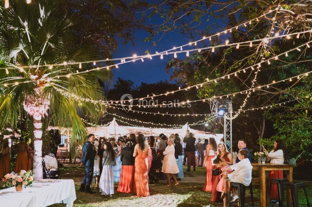 Groupe de personnes réunies dans un jardin éclairé par des guirlandes lumineuses, en soirée festive.