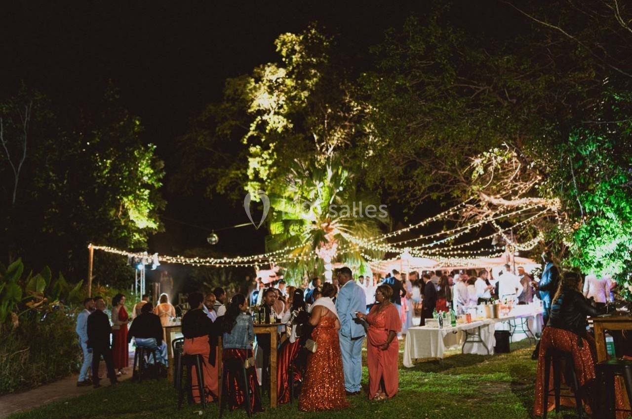 Groupe de personnes rassemblées dans un jardin éclairé par des guirlandes lumineuses lors d'un événement nocturne.
