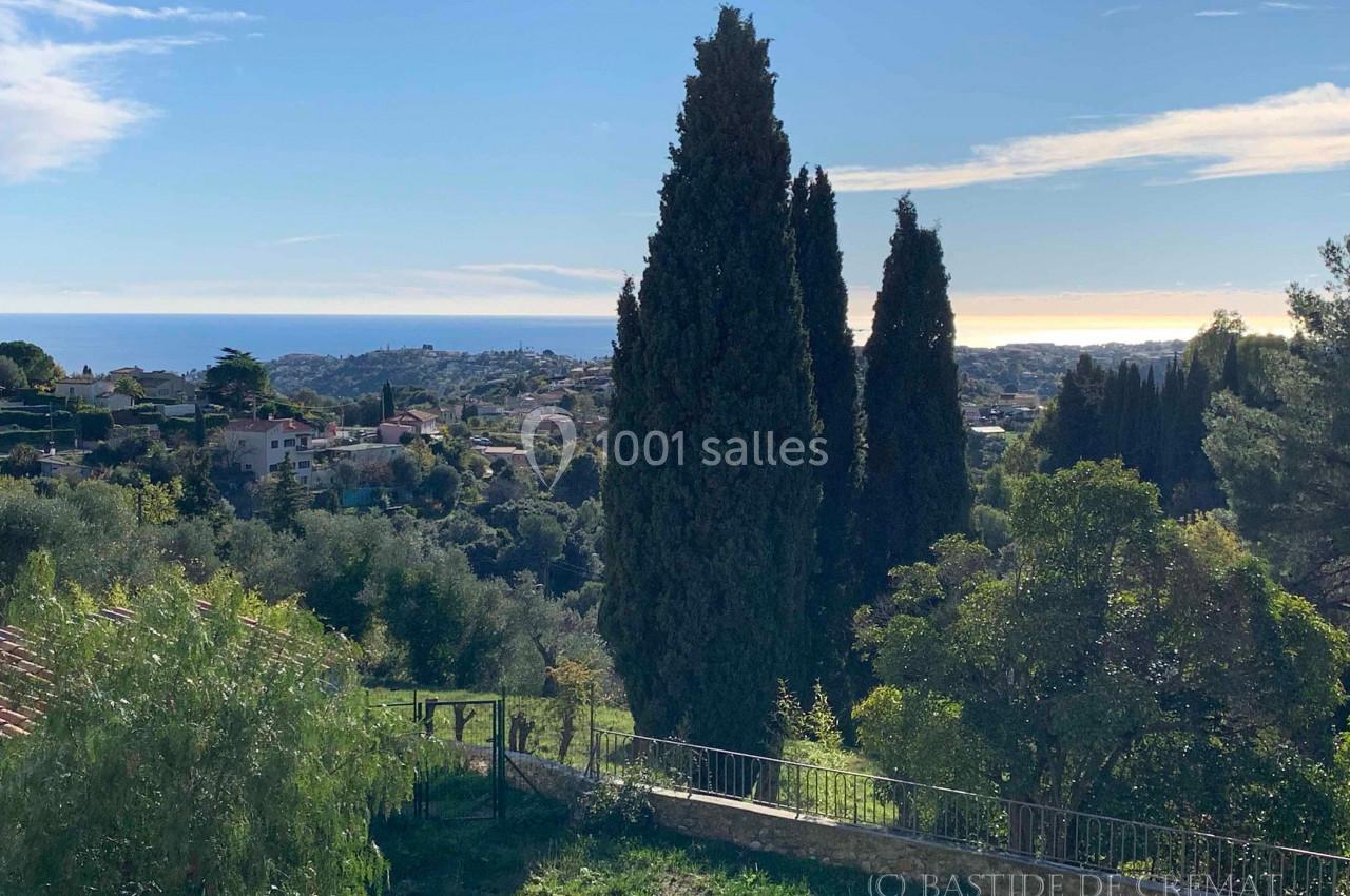 Vue sur un paysage méditerranéen avec des cyprès, des collines verdoyantes et la mer à l'horizon sous un ciel dégagé.