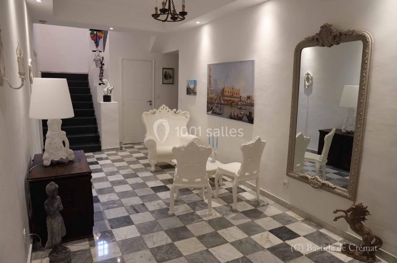 Hall d'entrée lumineux avec sol en marbre, fauteuils blancs, miroir mural et escalier menant à l'étage.