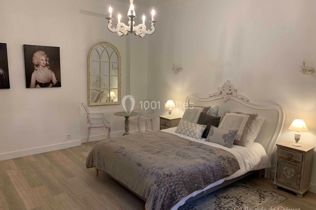 Chambre élégante avec lit double, lustre, miroir ancien, deux tables de chevet et éclairage doux.