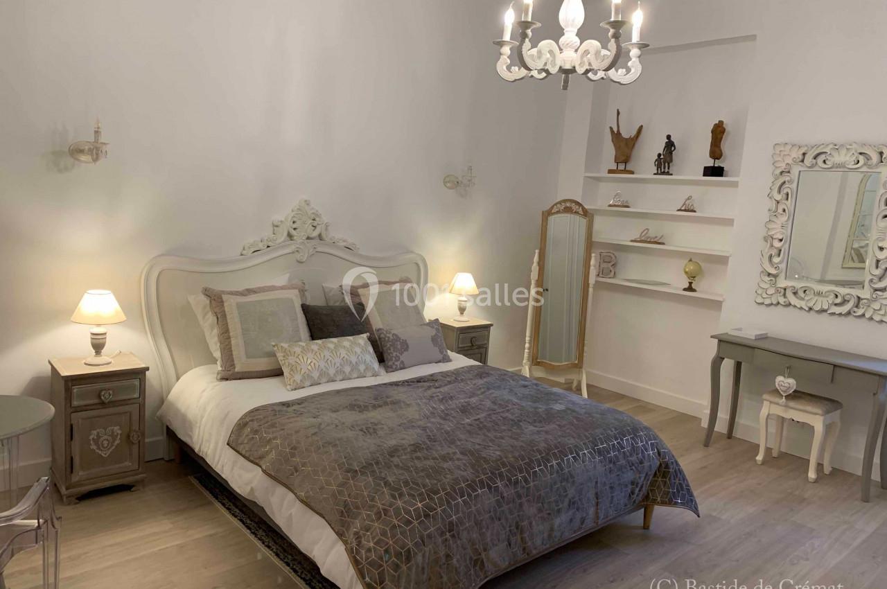 Chambre élégante avec lit double, décorée dans des tons neutres, éclairée par des lampes et un lustre.