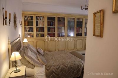 Chambre avec un lit double, éclairage doux et une grande bibliothèque en bois remplie de livres en arrière-plan.