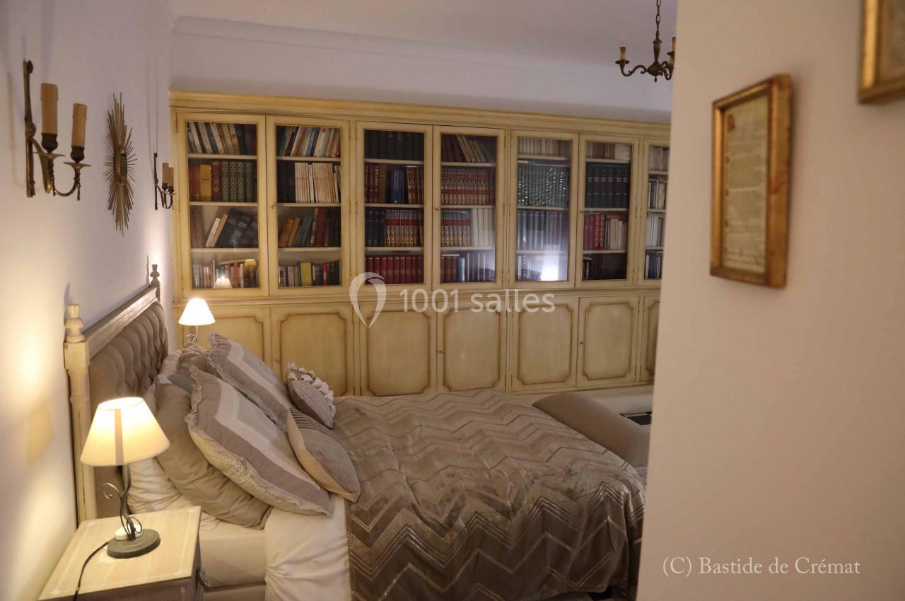 Chambre avec un lit double, éclairage doux et une grande bibliothèque en bois remplie de livres en arrière-plan.