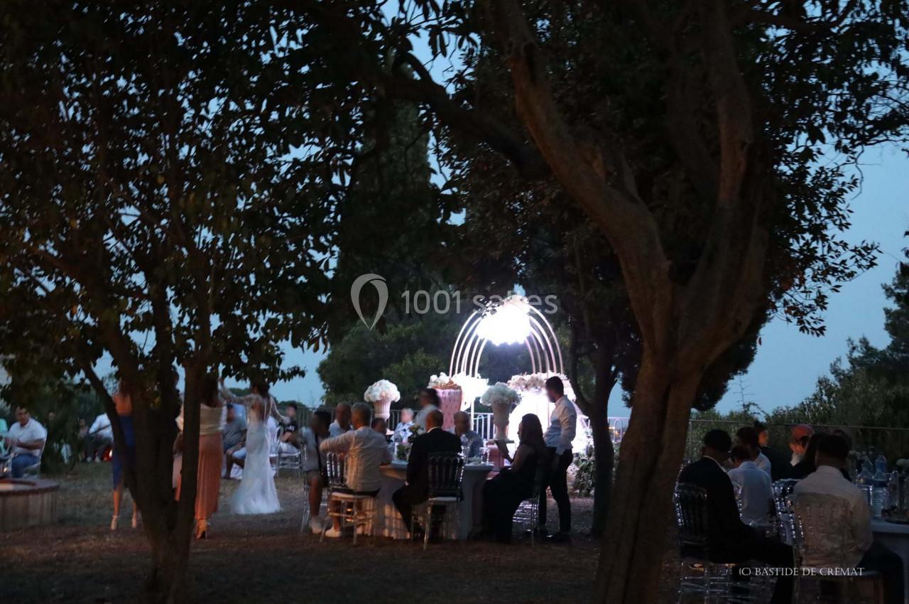 Cérémonie de mariage en plein air au crépuscule, avec des invités assis et un éclairage décoratif sous une arche.