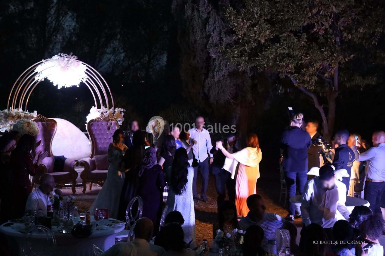 Des invités dansent et discutent lors d'une soirée en extérieur, avec une arche lumineuse et des fauteuils décoratifs en…