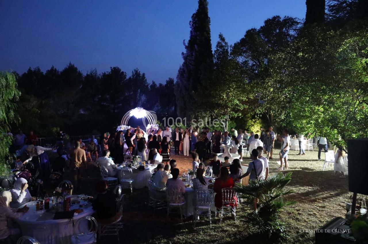 Groupe de personnes rassemblées en soirée dans un jardin éclairé, avec des tables dressées et des arbres en arrière-plan.