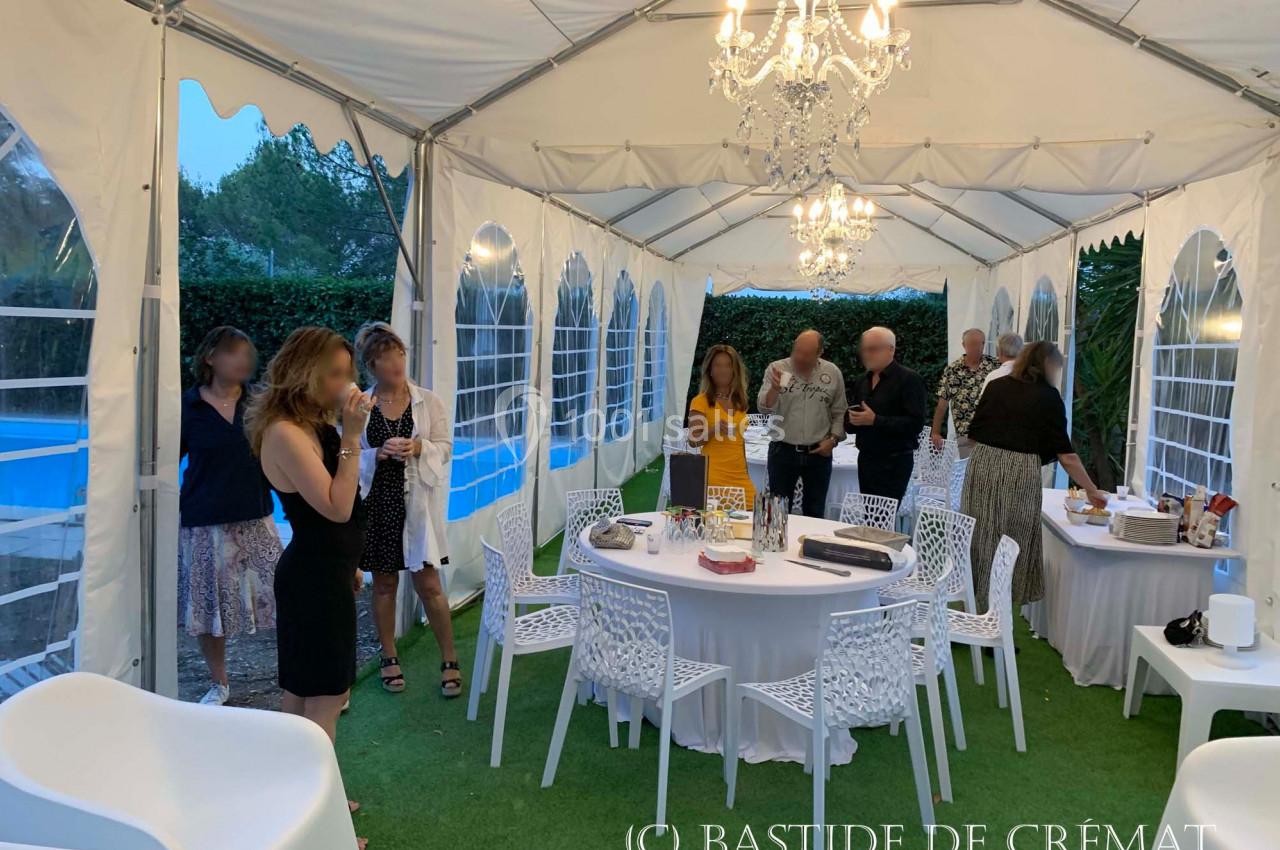 Groupe de personnes discutant sous une tente blanche éclairée, avec tables dressées et vue sur une piscine en arrière-plan.