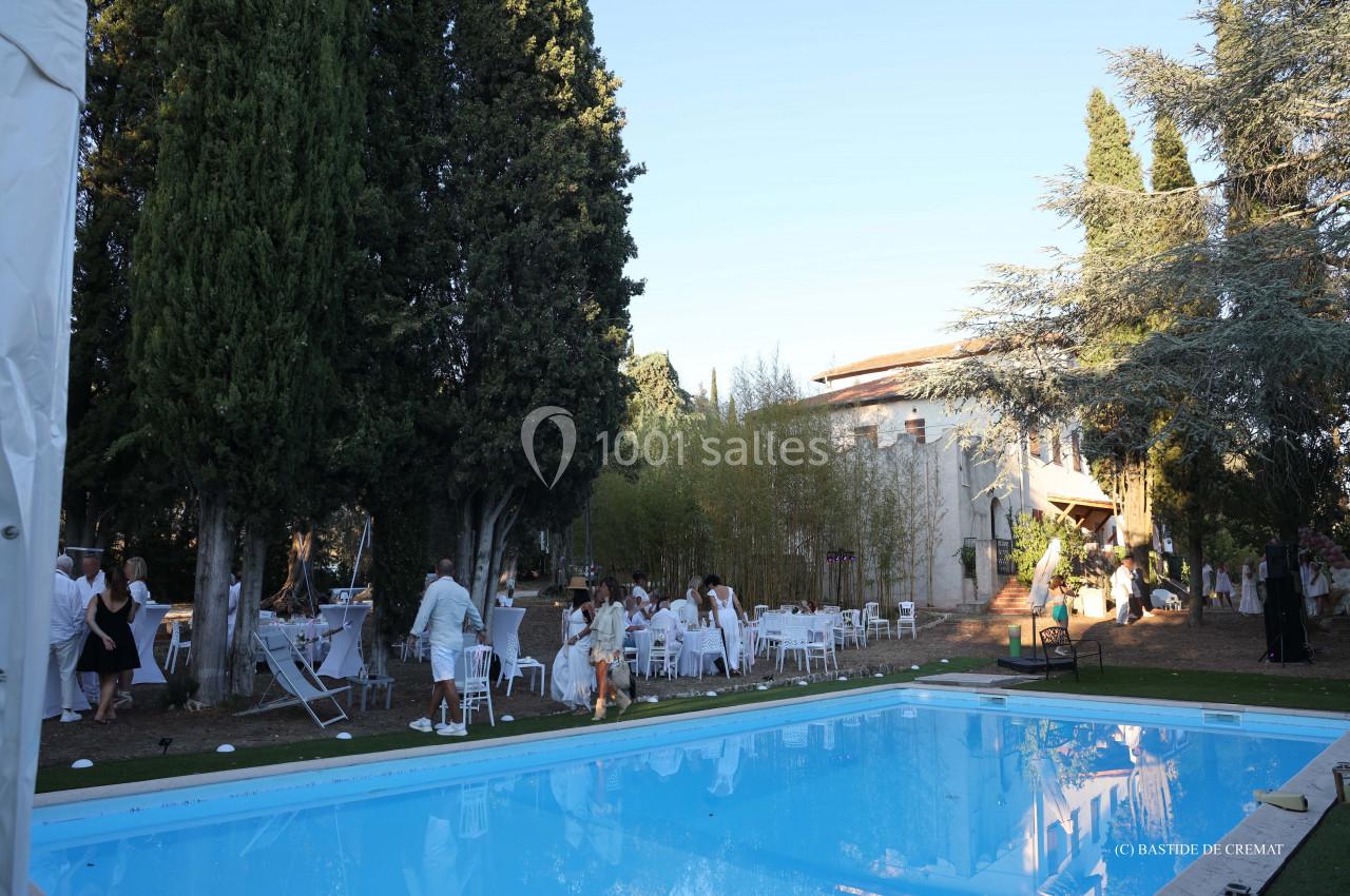 Personnes rassemblées dans un jardin près d'une piscine, entouré de grands arbres et d'un bâtiment en arrière-plan.