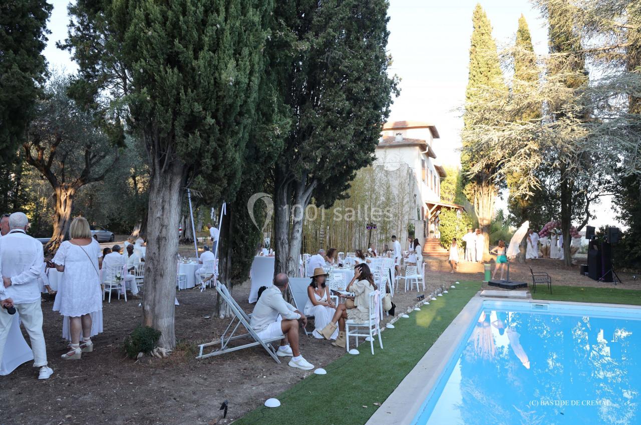 Groupe de personnes en tenue blanche réunies dans un jardin près d'une piscine, entouré d'arbres et d'une maison.