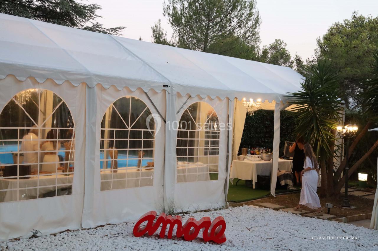 Tente blanche avec fenêtres transparentes, entourée de végétation, décorée avec le mot ’amore’ en rouge au sol.