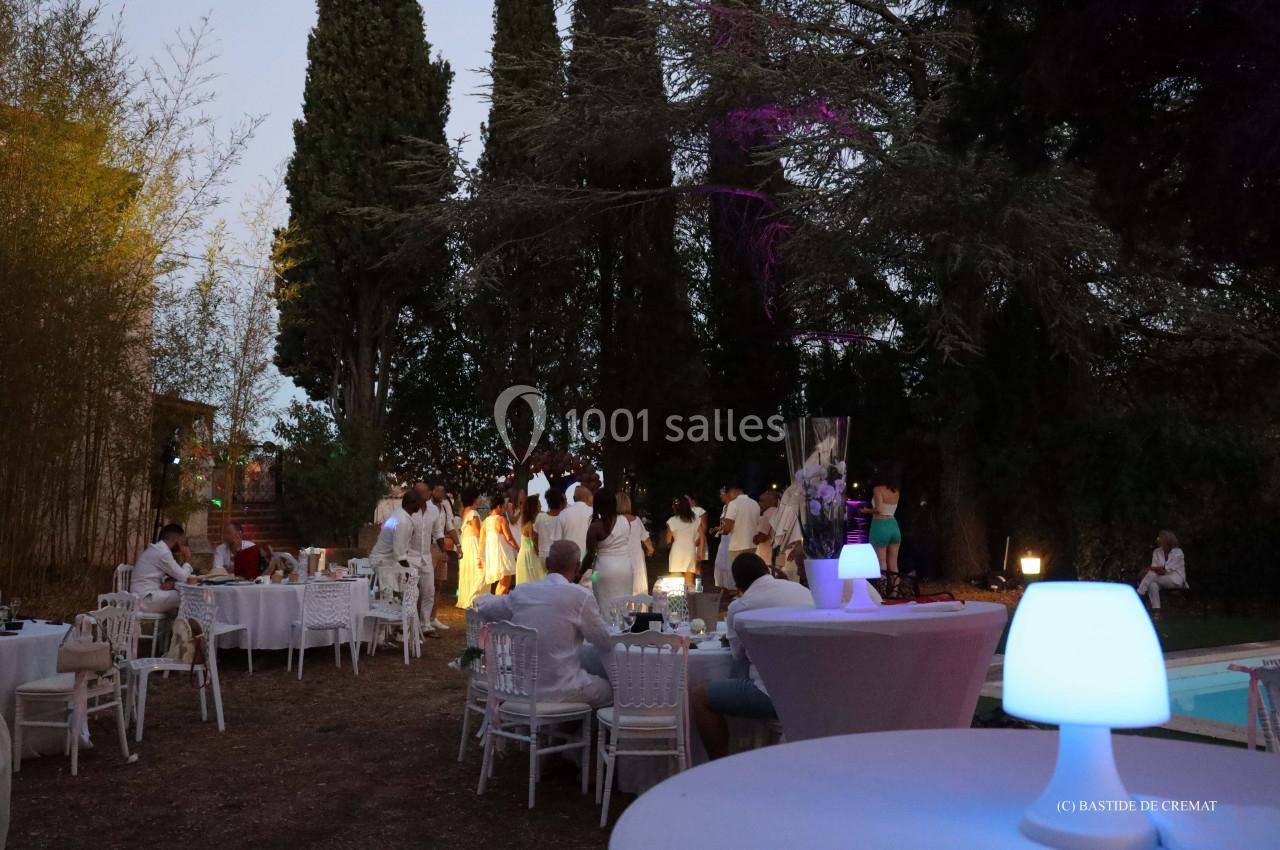 Groupe de personnes en tenue blanche dans un jardin éclairé, entouré de tables dressées et d'arbres.