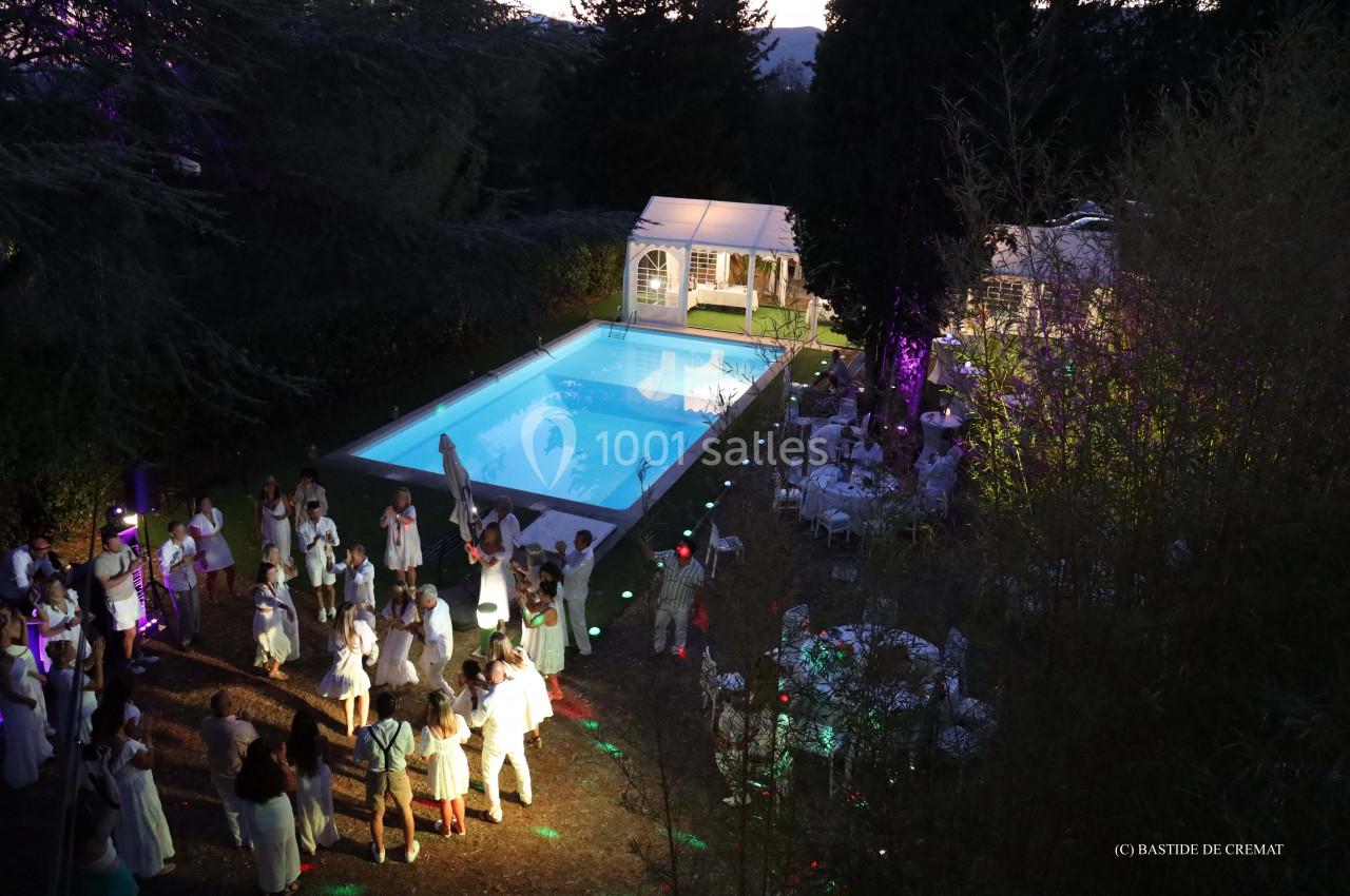 Vue aérienne d'une réception en soirée avec piscine éclairée, invités en blanc et tables dressées sous des tentes.