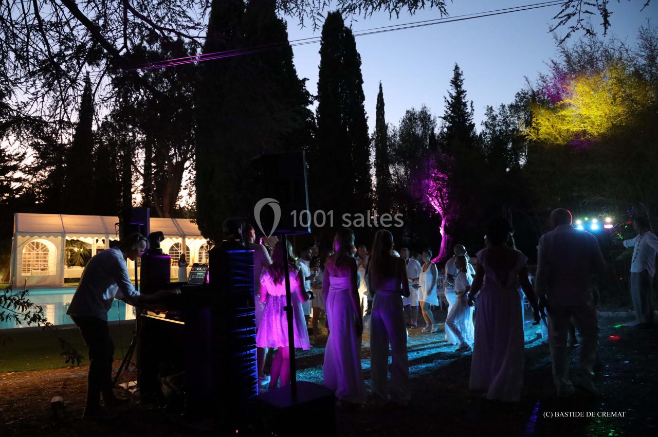 Groupe de personnes dansant en soirée en extérieur, éclairées par des lumières colorées près d'une piscine et d'arbres.