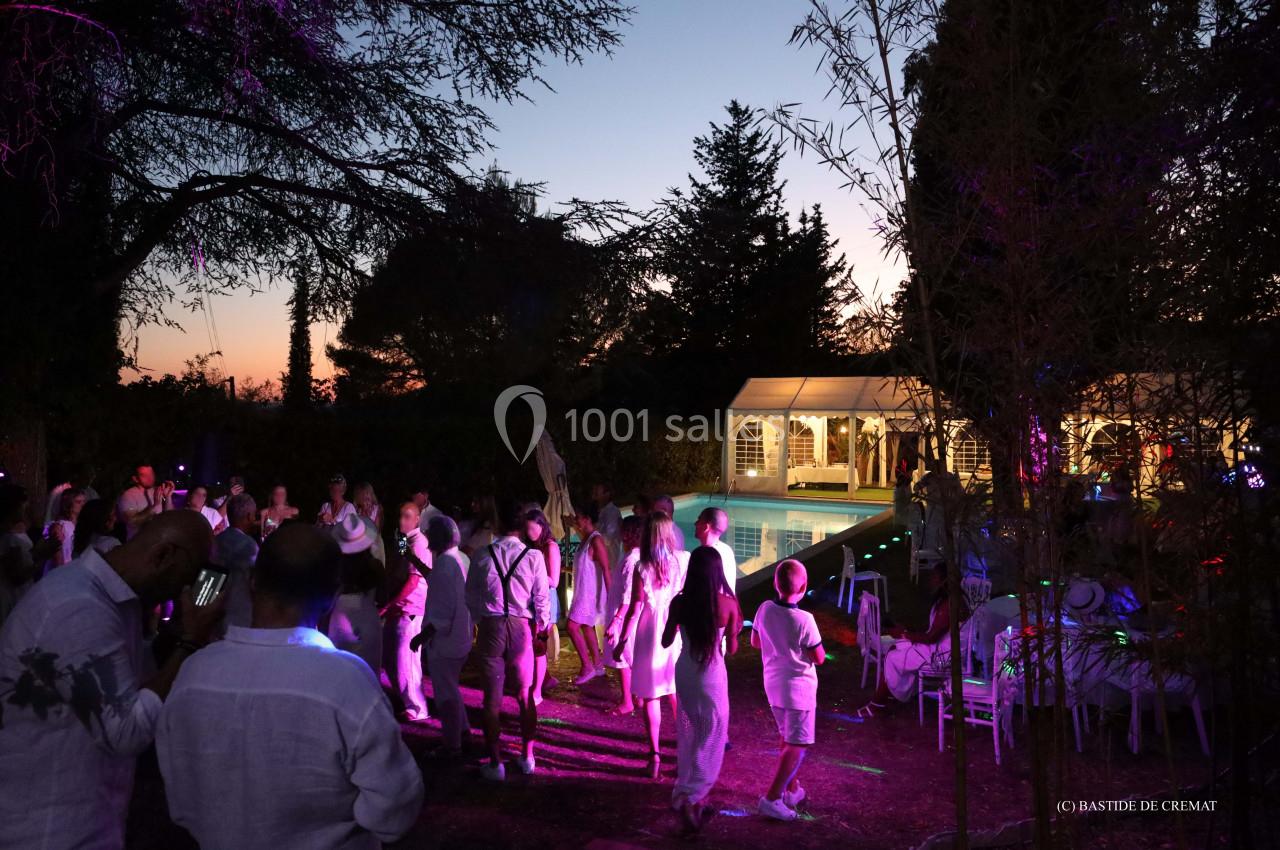 Groupe de personnes dansant en soirée près d'une piscine éclairée, entourée d'arbres au crépuscule.