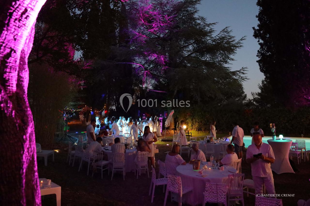 Personnes vêtues de blanc participant à une soirée en plein air, entourées d'arbres illuminés par des lumières colorées.