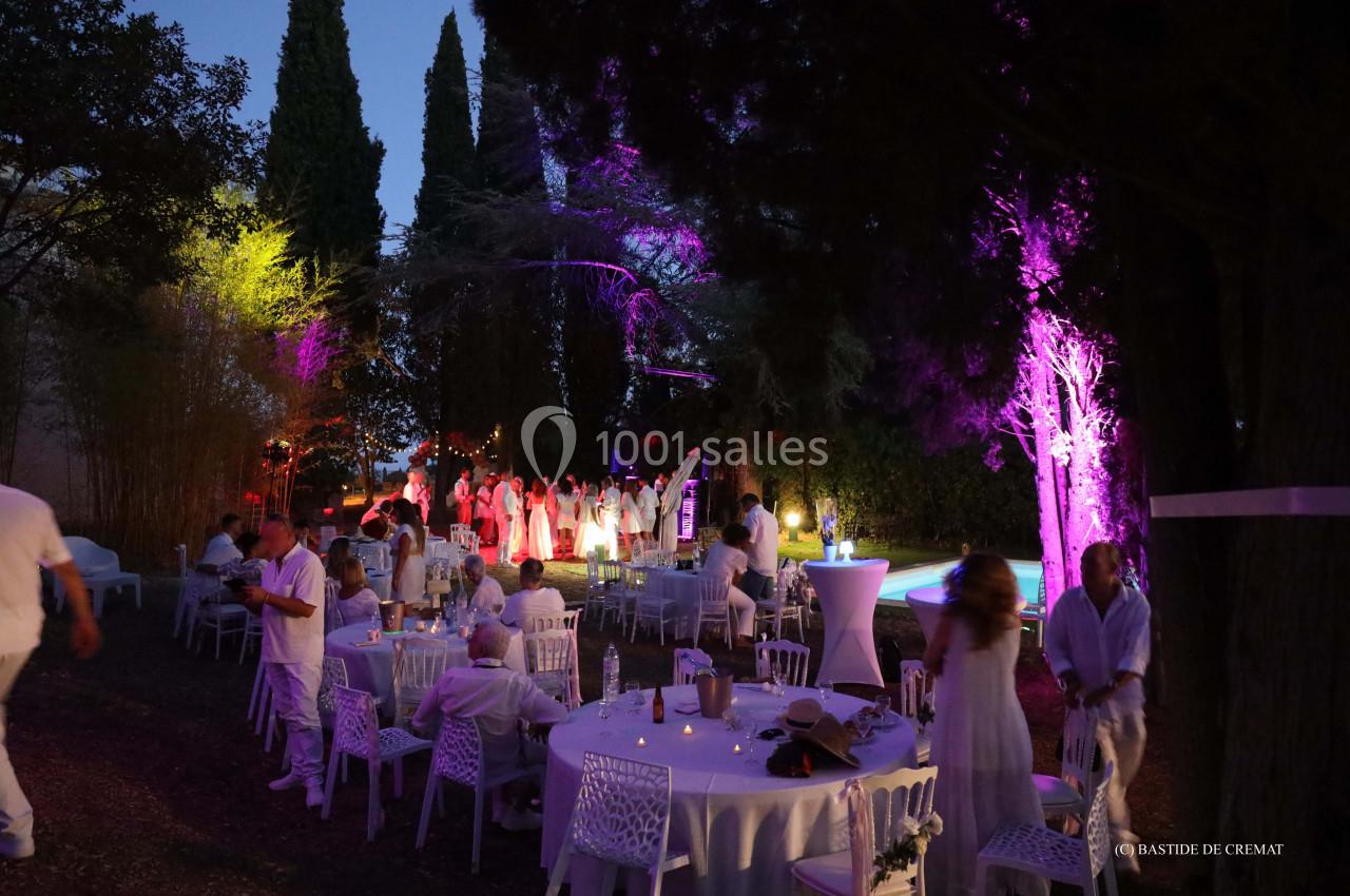 Groupe de personnes en tenue blanche lors d'une soirée en plein air, entourées d'arbres illuminés de lumières colorées.