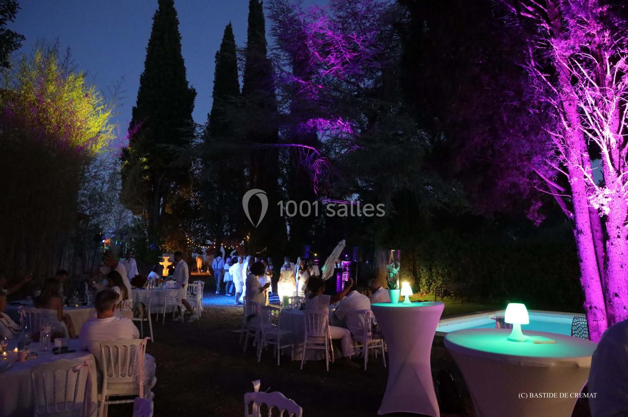 Soirée en extérieur avec des invités assis et debout, éclairages colorés et piscine visible à droite.