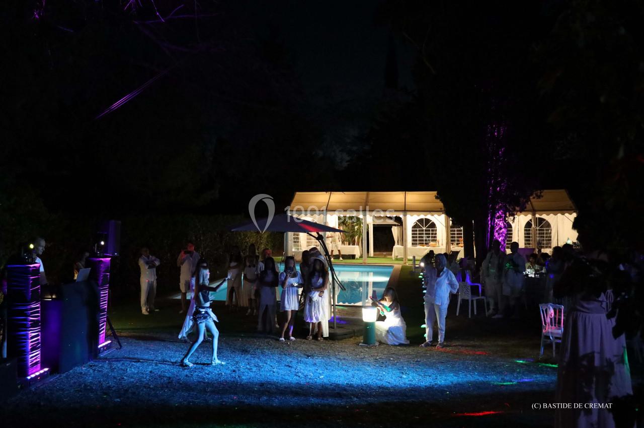 Groupe de personnes en tenue blanche rassemblées autour d'une piscine éclairée lors d'un événement nocturne en extérieur.