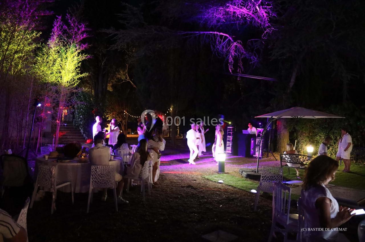 Personnes vêtues de blanc dans un jardin éclairé par des lumières colorées, lors d'un événement en soirée.