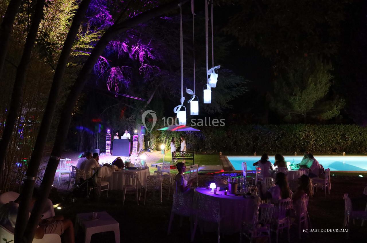 Des convives dînent en extérieur près d'une piscine éclairée, avec des décorations lumineuses et une ambiance nocturne…