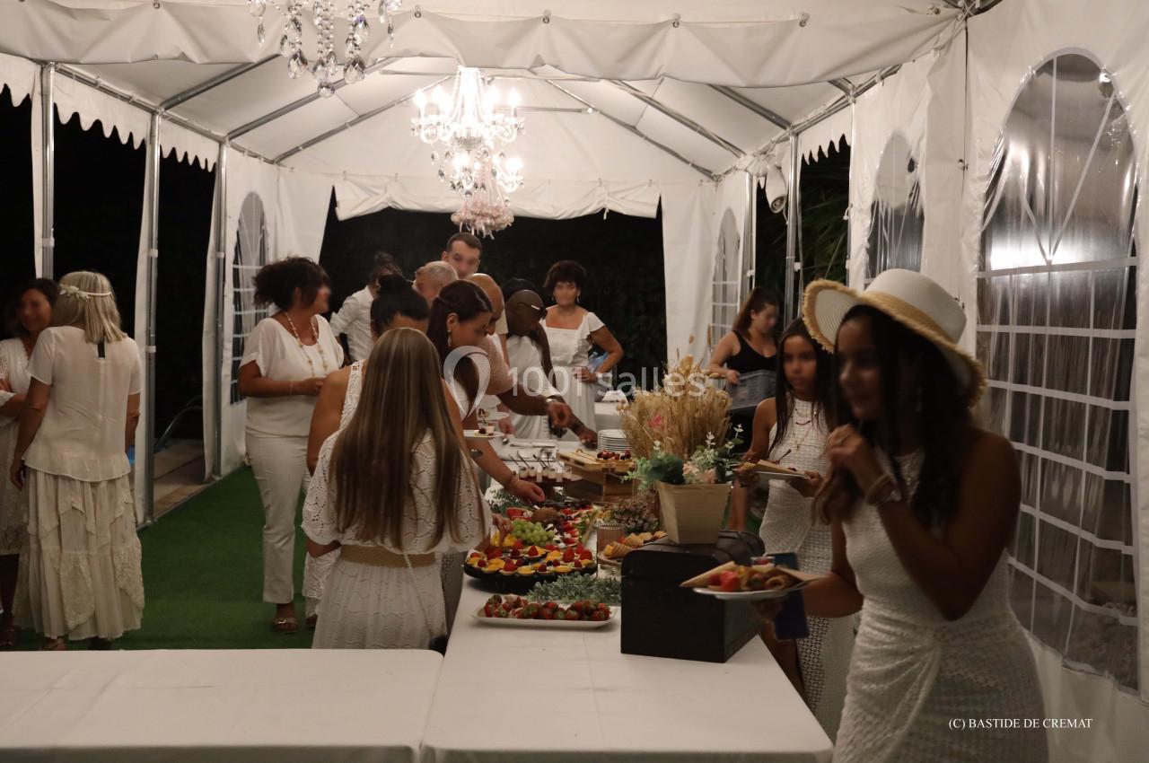 Des personnes en tenue blanche se servent à un buffet sous une tente éclairée par des lustres.