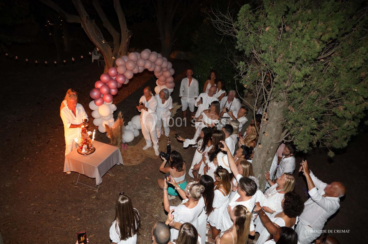Un groupe de personnes en tenue blanche assiste à un événement nocturne avec une décoration de ballons et des lumières.