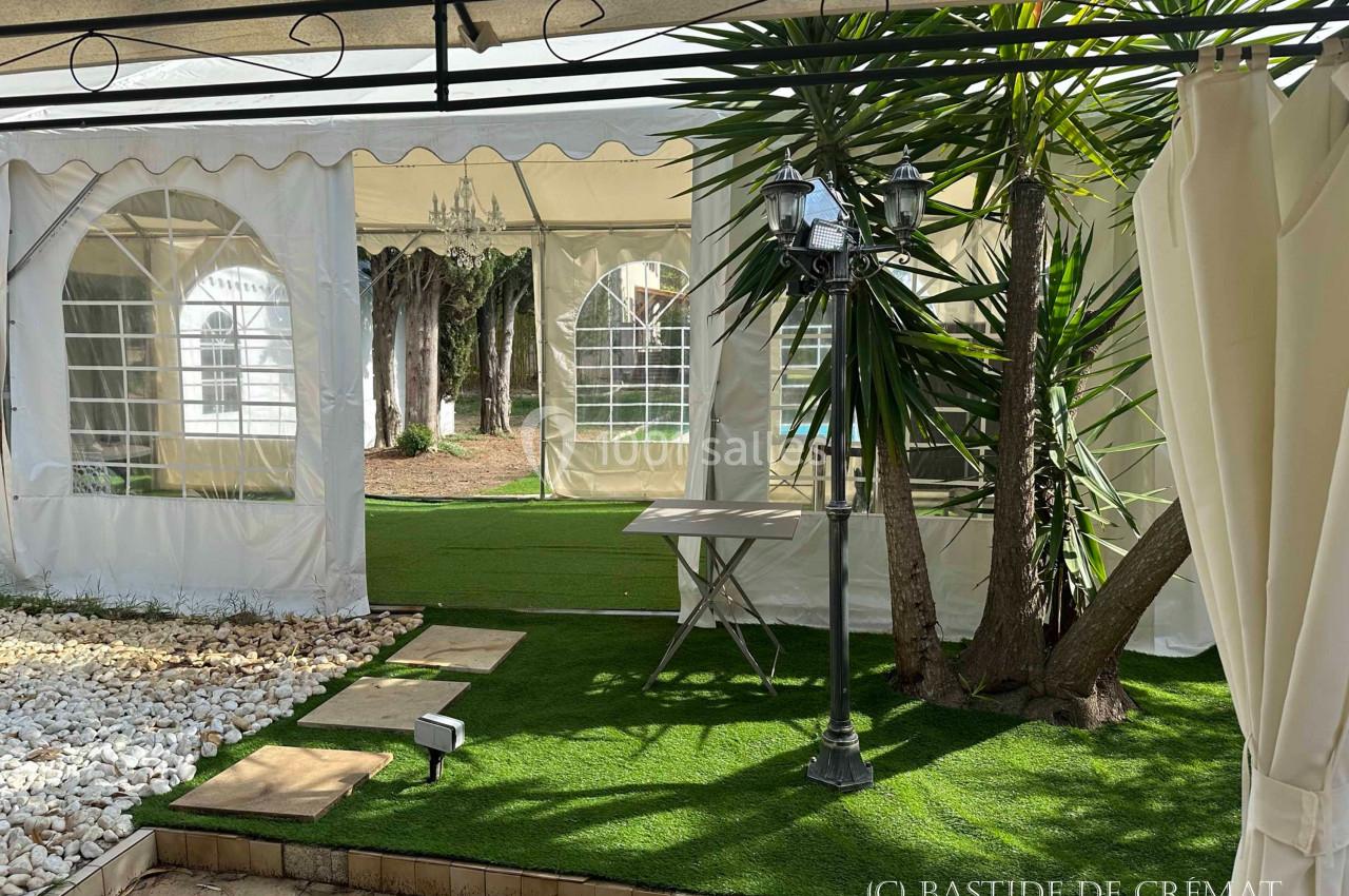 Vue d'une terrasse couverte avec des tentes blanches, un lampadaire, des plantes et un sol en gazon synthétique.