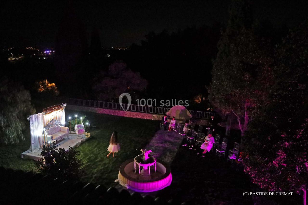 Vue nocturne d'un jardin éclairé avec des lumières violettes, des invités assis et une décoration lumineuse.