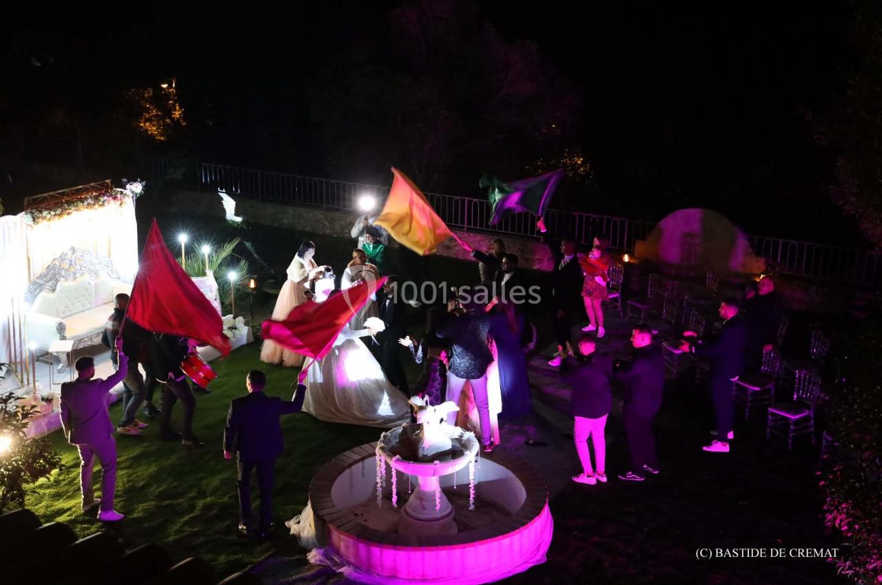Des personnes dansent et agitent des drapeaux colorés lors d'une célébration nocturne en extérieur, près d'une fontaine…
