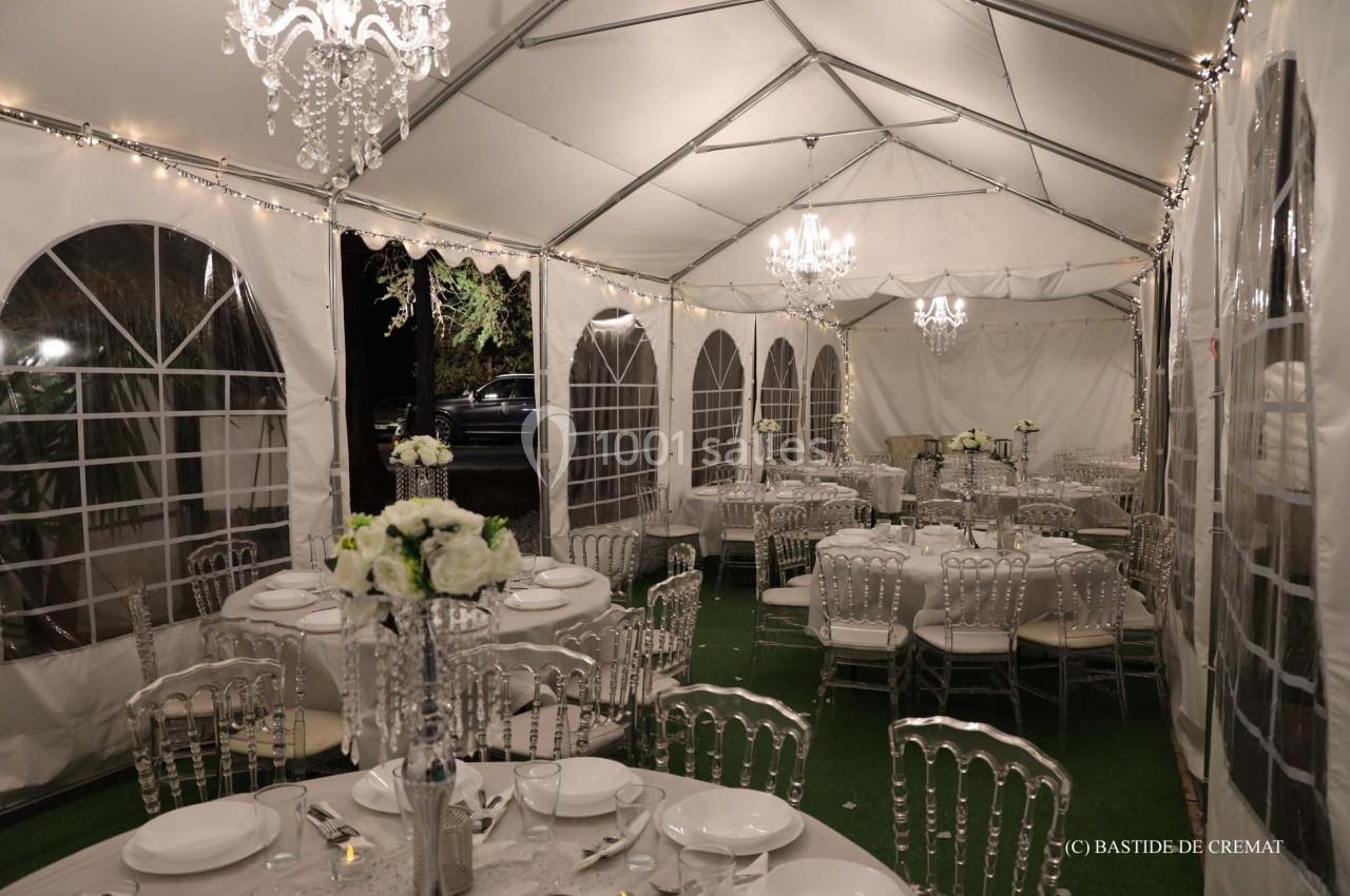 Intérieur d'une tente élégamment décorée avec des tables dressées, des chaises transparentes et des lustres suspendus.