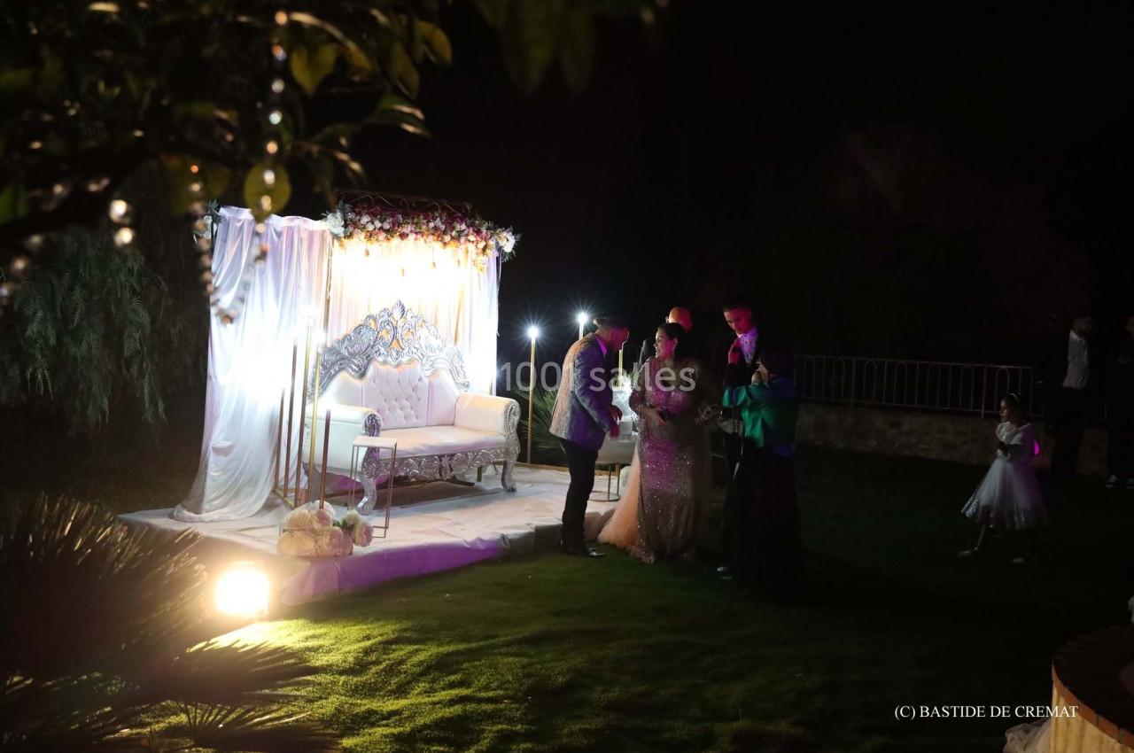 Un espace décoré avec un canapé et des rideaux illuminés, entouré de personnes dans un jardin de nuit.