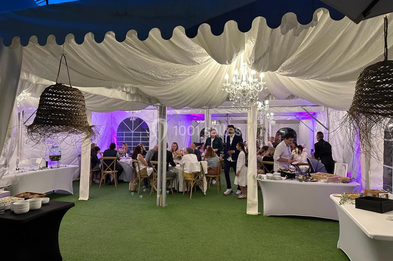Dîner convivial sous une tente éclairée, avec des invités assis à des tables et un buffet sur les côtés.