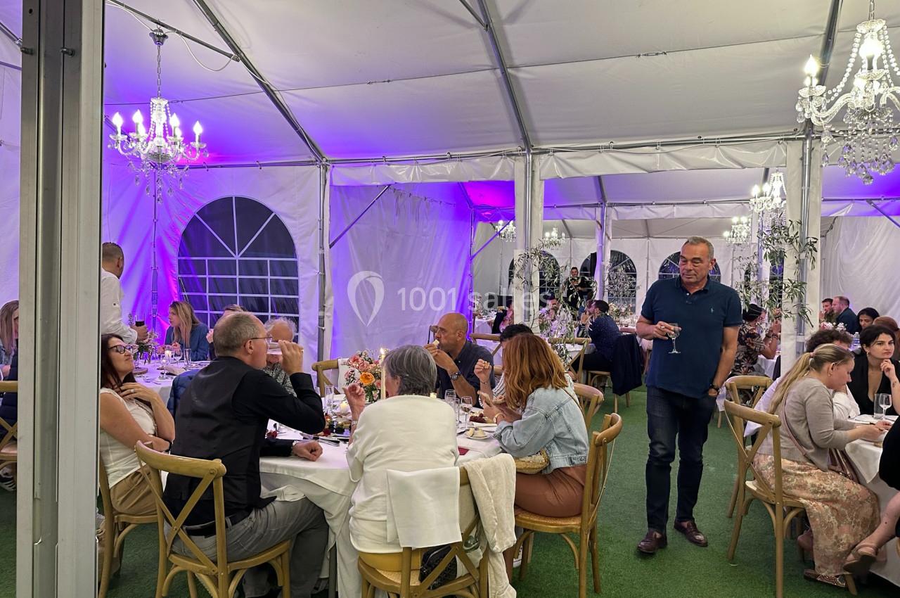 Personnes assises à des tables rondes dans une tente éclairée, décorée de lustres et de lumières violettes.