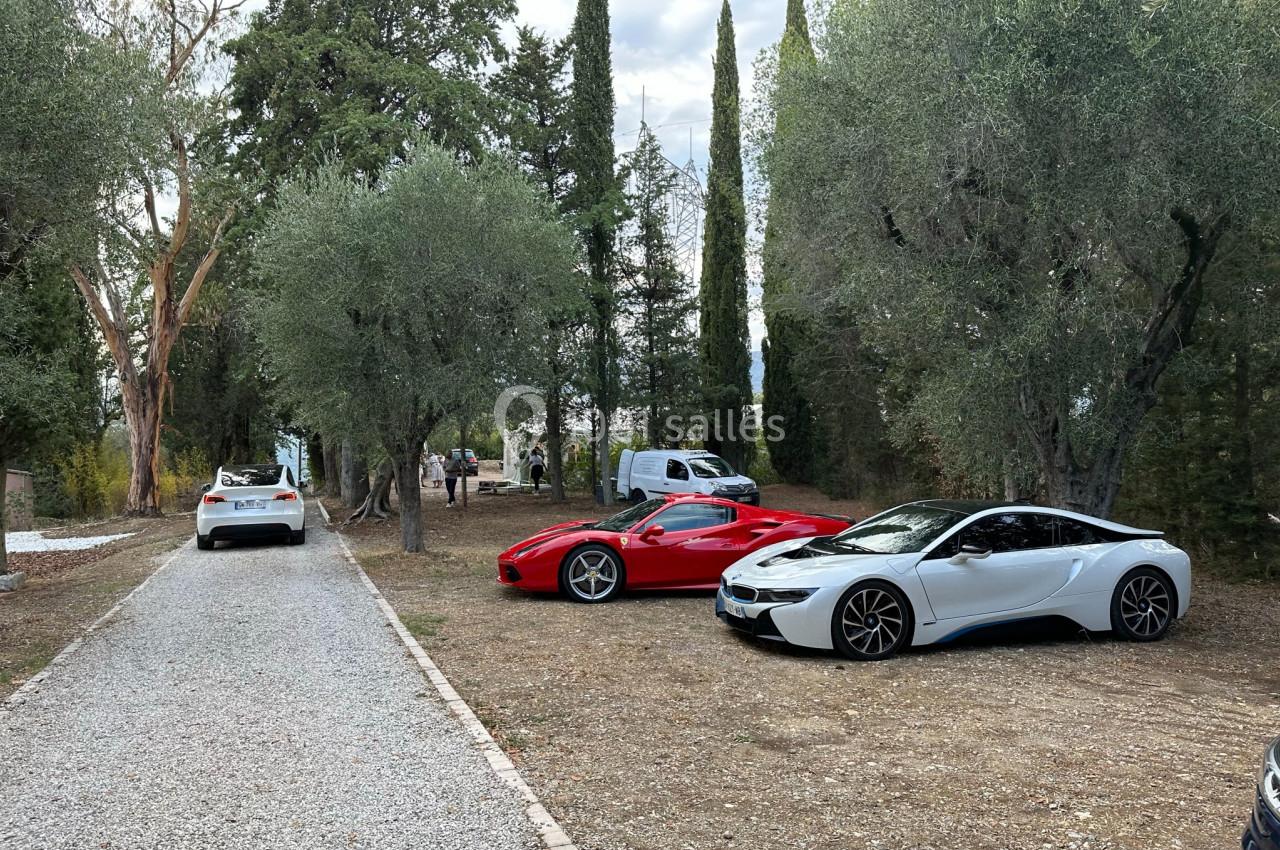 Deux voitures de sport, une rouge et une blanche, stationnées sur un terrain entouré d'arbres et d'une allée gravillonnée.