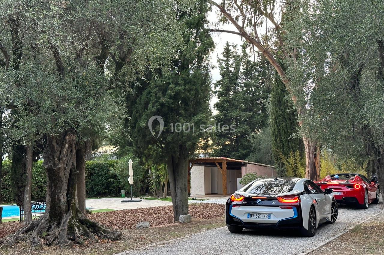 Deux voitures de sport garées sur une allée bordée d'arbres, près d'une piscine et d'un bâtiment en arrière-plan.