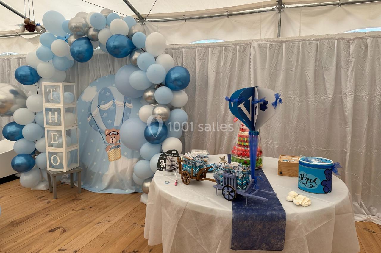 Décoration de fête avec arche de ballons bleus et blancs, table garnie de bonbons et éléments personnalisés.