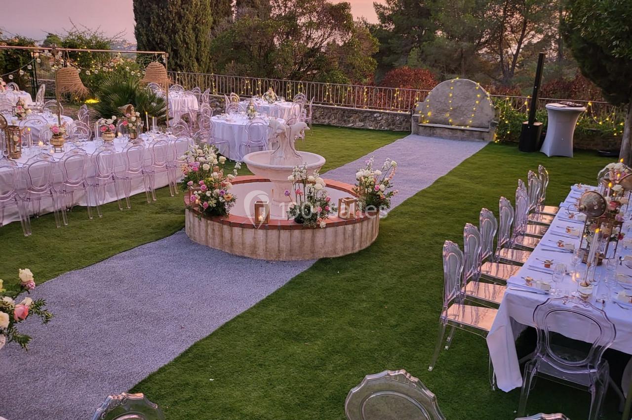 Allée centrale bordée de tables décorées pour un événement en plein air, avec pelouse et coucher de soleil en arrière-plan.