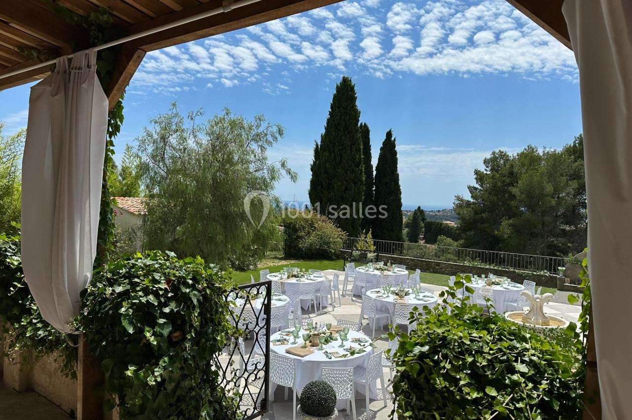 Tables dressées en extérieur sous un ciel bleu, entourées de verdure et partiellement abritées par une pergola.