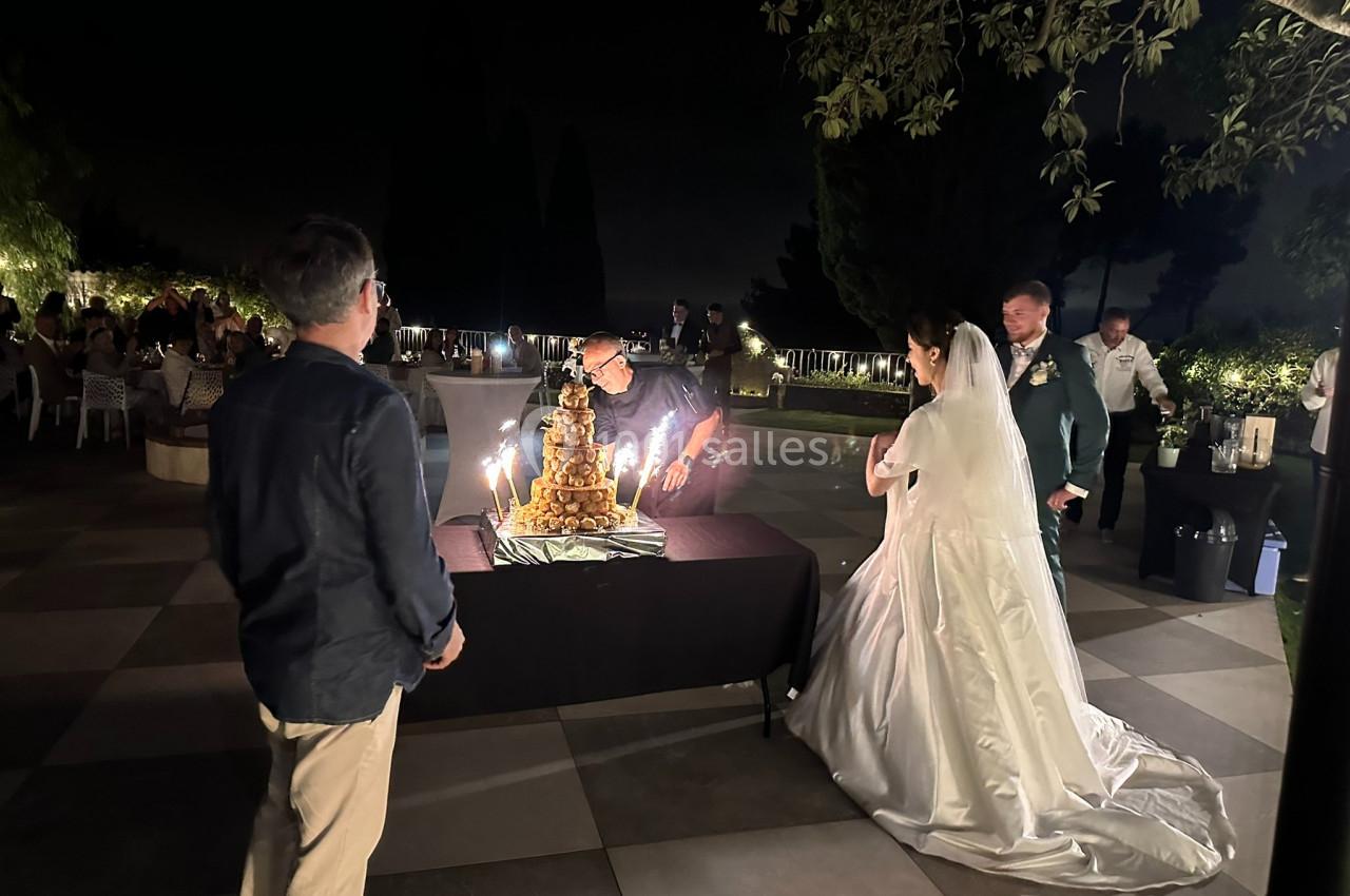 Un couple de mariés observe un serveur allumer les bougies d'une pièce montée lors d'une réception en soirée.