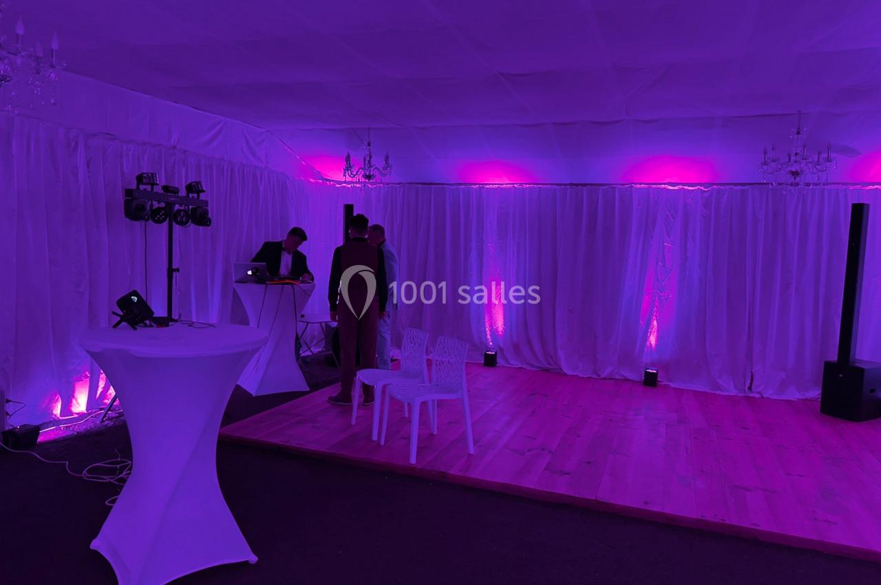 Salle décorée avec des rideaux blancs, éclairée par des lumières roses, avec une table haute et un espace DJ.